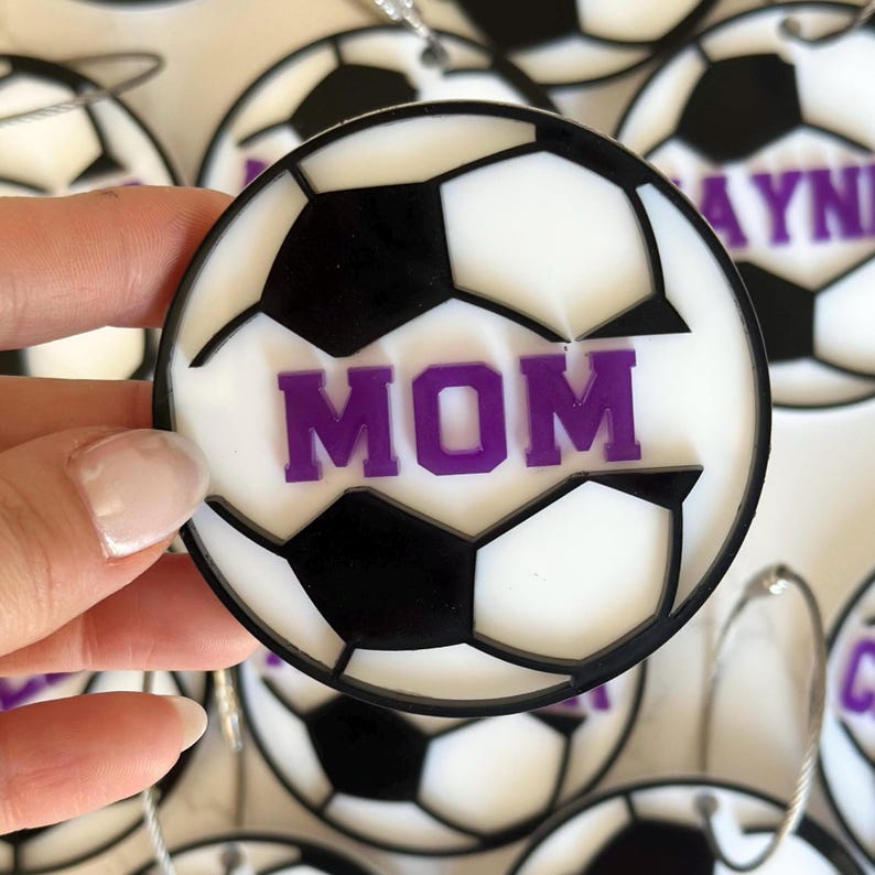 Op de afbeelding: Witte en zwarte voetbal ornament met een paarse "MOM" inscriptie.