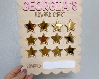 May include: A wooden reward chart with the name "GEORGIA'S" in pink letters. The chart has 15 gold star stickers and a blank space for a reward.