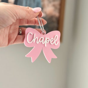 May include: A pink bow with a white "Chapel" inscription, hanging from a gray string.