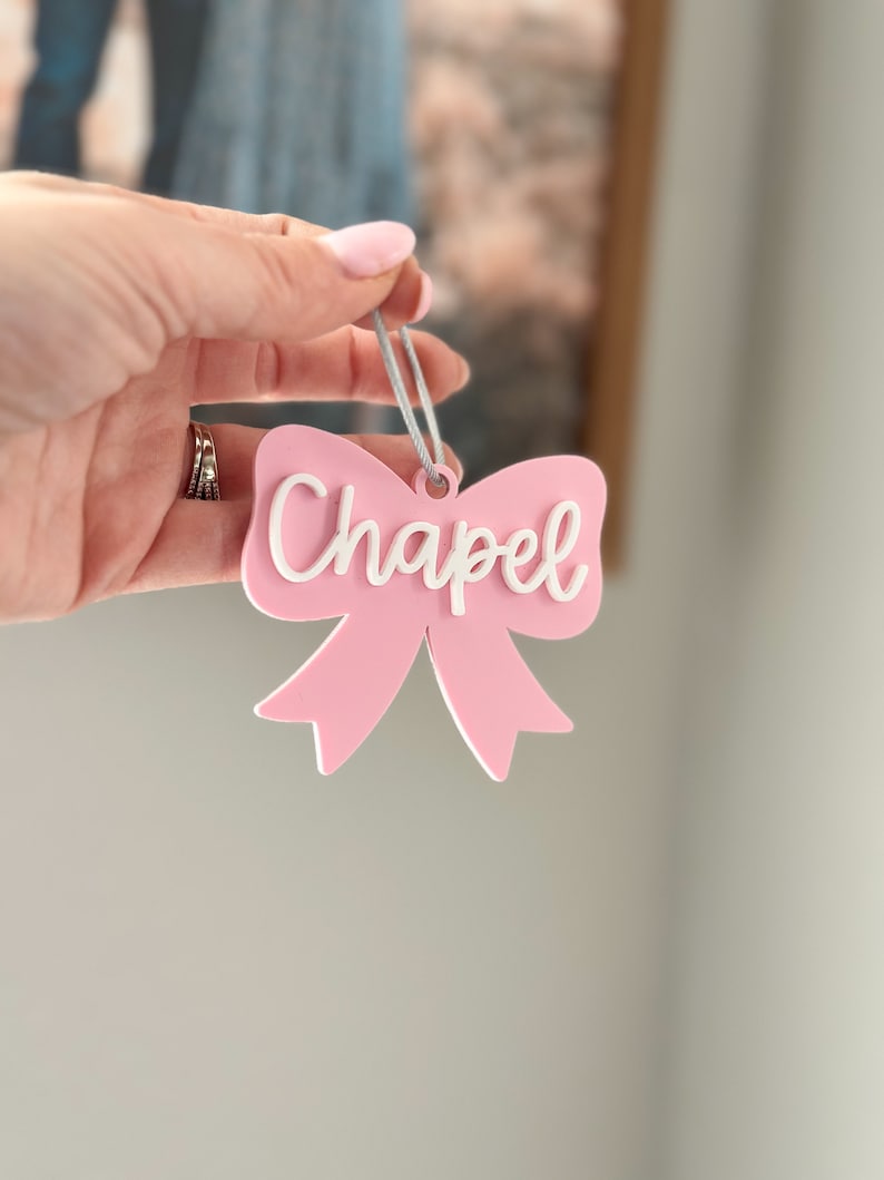 May include: A pink bow with a white "Chapel" inscription, hanging from a gray string.