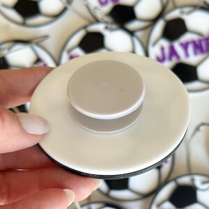 Op de afbeelding: Een witte plastic voetbal sleutelhanger met een zwart-wit voetbal ontwerp. De sleutelhanger heeft een witte plastic ring en een witte plastic knop aan de achterkant.