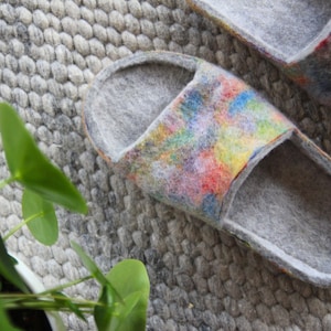 May include: A pair of grey felt slippers with a colourful abstract design on the top. The slippers are open-toed and have a simple, comfortable design.