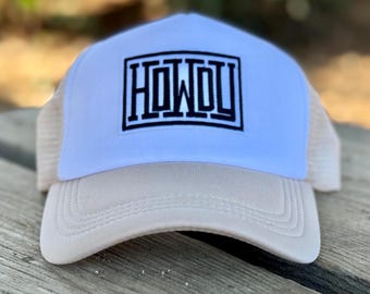 May include: A white and beige trucker hat with a black and white "HOWDY" logo embroidered on the front.