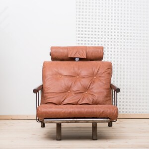 May include: A brown leather armchair with a tufted back and a headrest. The chair has a metal frame and wooden arms.