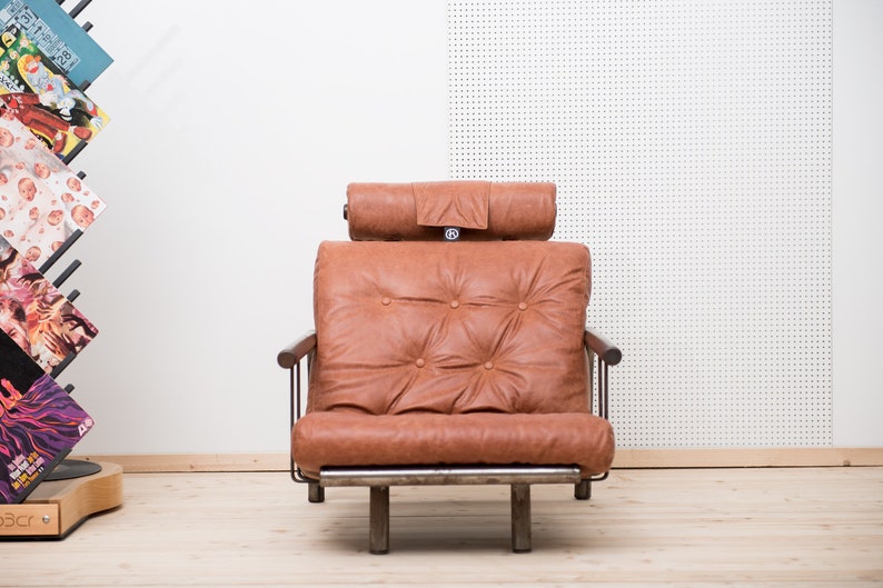 May include: A brown leather armchair with a tufted back and a headrest. The chair has a metal frame and wooden arms.
