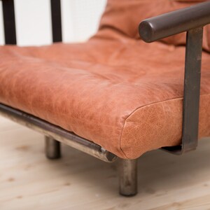 May include: A brown leather armchair with a metal frame. The chair has a simple design with a wide seat and a low back.