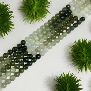 May include: A strand of round, green and white jade beads. The beads are graduated in size, with the largest beads at the center of the strand and the smallest beads at the ends. The beads are smooth and polished.