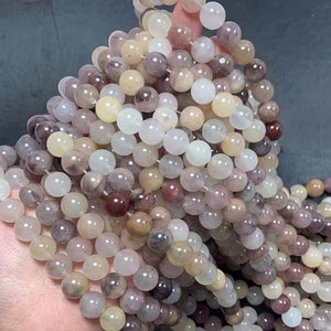 May include: A strand of round, translucent gemstone beads in shades of white, pink, and brown. The beads have a natural, polished finish and are strung on a clear elastic cord.