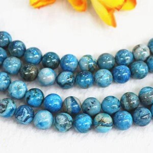 Puede incluir: Primer plano de hileras de cuentas redondas y pulidas en tonos azules y turquesas. Las cuentas tienen un aspecto veteado, con variaciones de color y patrón. Las cuentas están ensartadas, para un collar o pulsera.