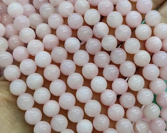 Puede incluir: Una hebra de cuentas redondas de piedra preciosa de color rosa pálido. Las cuentas son lisas y tienen un brillo sutil.