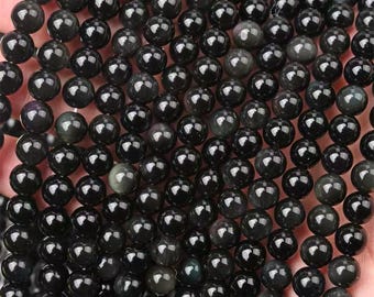 May include: Close-up of a collection of polished, round, black obsidian beads. The beads have a glossy finish and reflect light, showcasing subtle variations in color and texture. These beads are ideal for jewelry making.