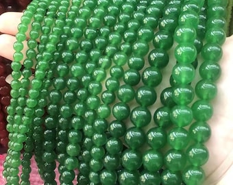May include: Close-up of multiple strands of vibrant, emerald green beads. The beads are spherical and polished, with varying sizes. They are strung together, likely for jewellery or decorative purposes.