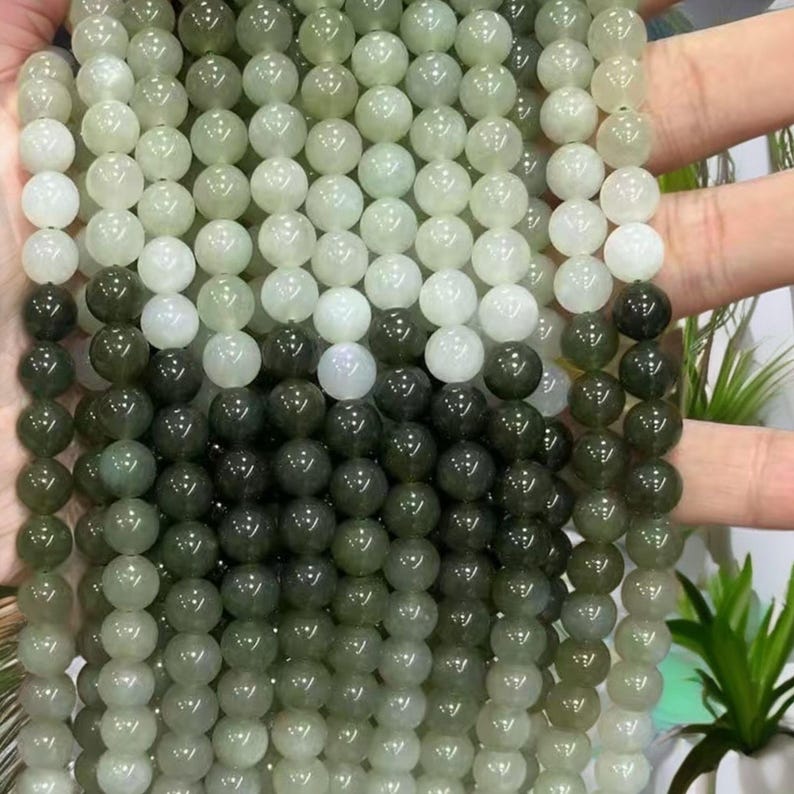 May include: A strand of round, green and white jade beads. The beads are graduated in color, with the lightest beads at the top and the darkest beads at the bottom.
