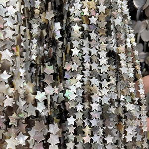 Puede incluir: Una hebra de cuentas de concha de estrella blanca iridiscente. Las cuentas están enhebradas en un cordón delgado y oscuro.