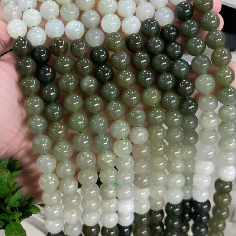 May include: A strand of round, green and white jade beads. The beads are graduated in size, with the larger beads at the top and the smaller beads at the bottom. The beads are strung on a clear elastic cord.