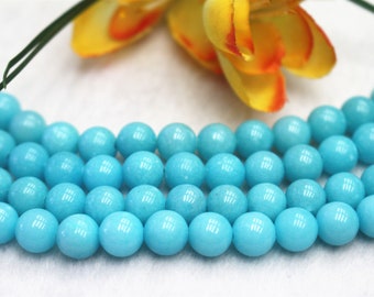 May include: A strand of turquoise blue round beads, each bead is smooth and polished. The beads are arranged in a row, with the top row slightly overlapping the bottom row.