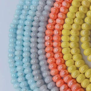 Peut inclure: Gros plan sur un brin de perles de verre colorées. Les perles sont disposées en arc-en-ciel, avec des perles bleues, grises, orange et jaunes. Les perles sont toutes rondes et ont une finition lisse et brillante.