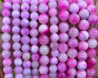 Puede incluir: Una hebra de cuentas redondas de color rosa y blanco. Las cuentas están hechas de un material translúcido con un ligero brillo.