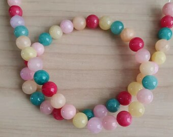 Puede incluir: Una hebra de cuentas redondas de colores en tonos rosa, amarillo, verde y rojo. Las cuentas están enhebradas en un cordón elástico transparente y están dispuestas en un patrón circular.
