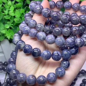 Può includere: Un set di braccialetti in pietre preziose blu e viola. I braccialetti sono fatti di perline rotonde e sono infilati su un elastico.