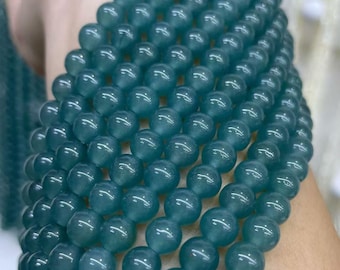 May include: A close-up of a strand of teal-colored beads. The beads are round and appear to be made of a smooth, polished material. The beads are strung together, forming a necklace or bracelet. The color is a deep, sea-green hue.