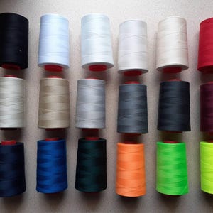 May include: A selection of thread spools in a variety of colours, including black, white, red, and green. The spools are arranged in neat rows, showcasing a range of colours suitable for sewing and crafting projects. The image highlights the variety of thread colours available.
