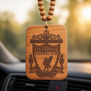 May include: A wooden car air freshener featuring the Liverpool Football Club emblem, with the text "YOU'LL NEVER WALK ALONE" and "EST 1892". The rectangular freshener hangs from a string of wooden beads.