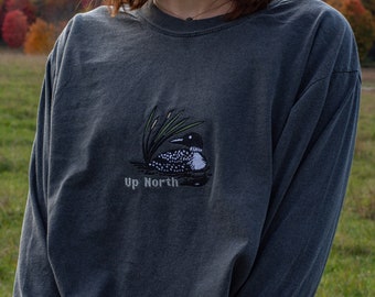 Puede incluir: Una camiseta de manga larga gris oscuro con un loon bordado y el texto "Up North".