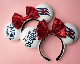 Könnte beinhalten: Weiße, paillettenbesetzte Mauseohren-Haarbänder mit roten Pailletten-Schleifen. Einige Ohren haben den Text "Disney Treasure" oder "Disney Destiny" in Blau. Andere Ohren haben ein Mickey Mouse-Logo und blaue Streifen.