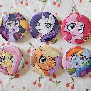 Op de afbeelding: Zes ronde, kleurrijke knopen met cartoonafbeeldingen van My Little Pony-personages. De personages zijn Twilight Sparkle, Rarity, Pinkie Pie, Fluttershy, Applejack en Rainbow Dash.