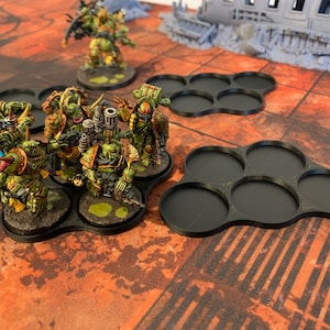 May include: A set of black plastic miniature bases for tabletop gaming. The bases are designed to hold multiple miniatures and have a unique, organic shape. The bases are arranged in a cluster, with some bases overlapping.