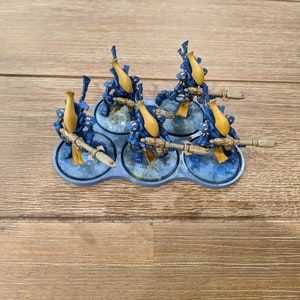 May include: Six blue and gold miniature figures with weapons, standing on a gray plastic base.