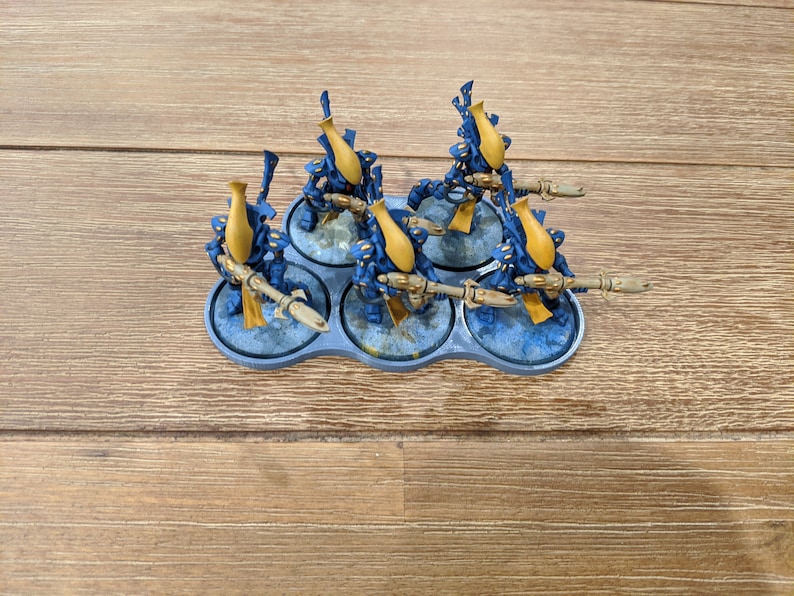 May include: Six blue and gold miniature figures with weapons, standing on a gray plastic base.