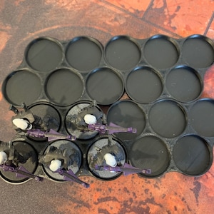 May include: A black plastic storage tray with 15 round compartments for holding miniature figures. Five miniature figures are shown in the compartments, painted in black and purple.
