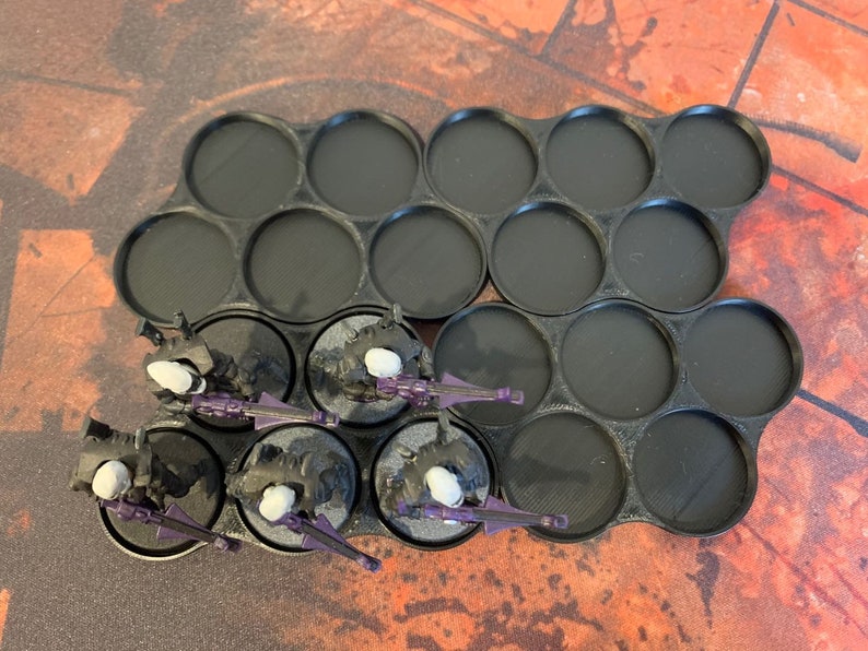 May include: A black plastic storage tray with 15 round compartments for holding miniature figures. Five miniature figures are shown in the compartments, painted in black and purple.