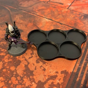 May include: Black plastic tray with six round compartments for holding miniature figures. The tray is designed to hold figures with a 25mm base.