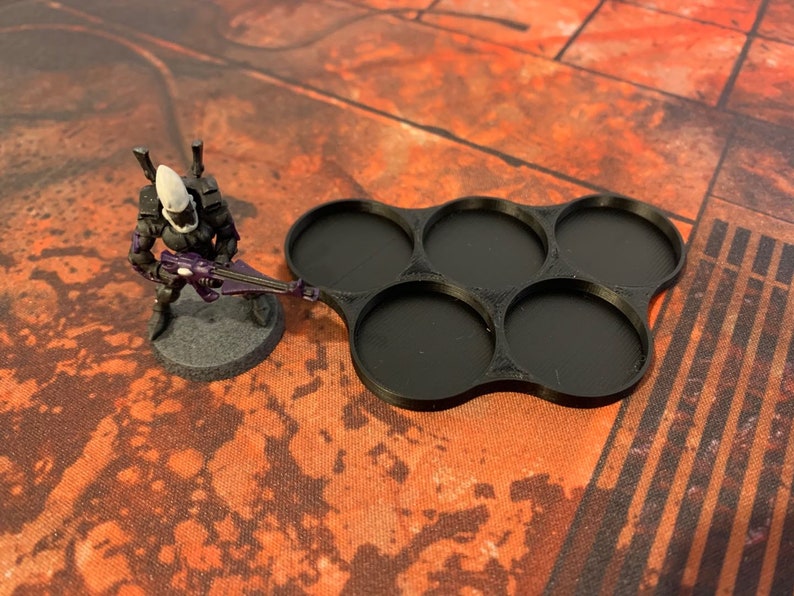 May include: Black plastic tray with six round compartments for holding miniature figures. The tray is designed to hold figures with a 25mm base.