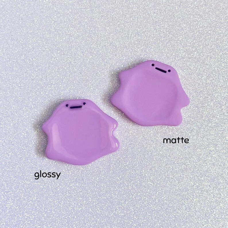 Pode incluir: Dois pingentes em forma de gota de cor lavanda com um pequeno detalhe de linha preta. Um pingente tem um acabamento brilhante e o outro tem um acabamento fosco. A palavra "glossy" est&aacute; escrita abaixo do pingente brilhante e "matte" est&aacute; escrita abaixo do pingente fosco.