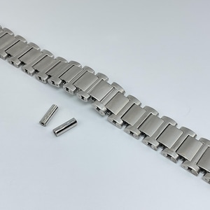 Peut inclure: Un bracelet de montre argenté avec une finition brossée et un fermoir. Le bracelet est composé de maillons individuels reliés par de petites goupilles. Deux goupilles supplémentaires sont incluses.