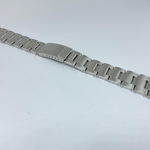 以下が含まれることがあります： ブラシ仕上げと留め具が付いたシルバーの腕時計バンド