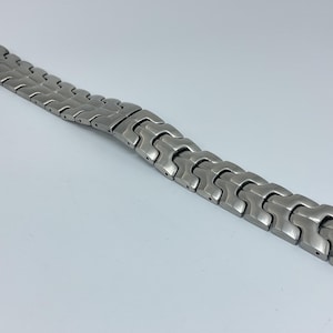 May include: A silver metal watch band with a unique interlocking design.