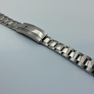 Puede incluir: Una correa de reloj de metal plateado con acabado cepillado y cierre.