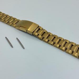 May include: Gold-tone watch band with a brushed finish and a deployment clasp. The band is made of metal and has a polished look. Two silver-tone spring bars are included.