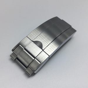 Puede incluir: Un cierre de pulsera de reloj de metal plateado con acabado cepillado.
