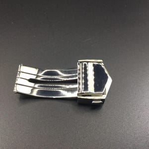 May include: A silver watch band clasp with a polished finish. The clasp has a three-piece design and a secure locking mechanism.