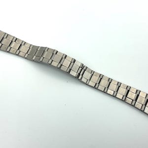May include: A silver metal watch strap with a brushed finish. The strap is made up of individual links that are connected together.