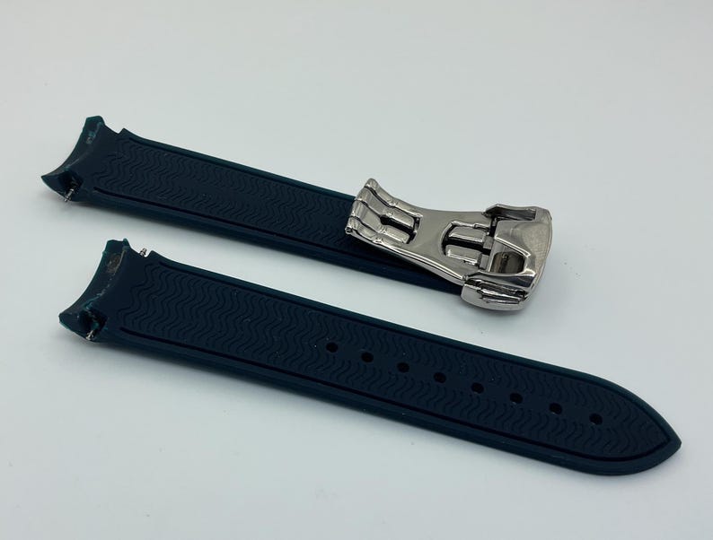 May include: A dark blue watch strap with a silver buckle. The strap has a textured surface and is made of rubber.
