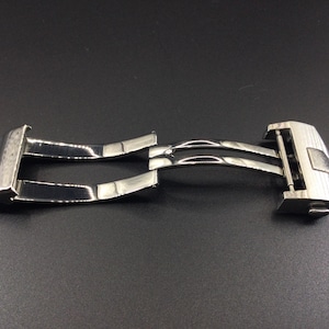 May include: A silver metal watch band clasp with a double-locking mechanism.