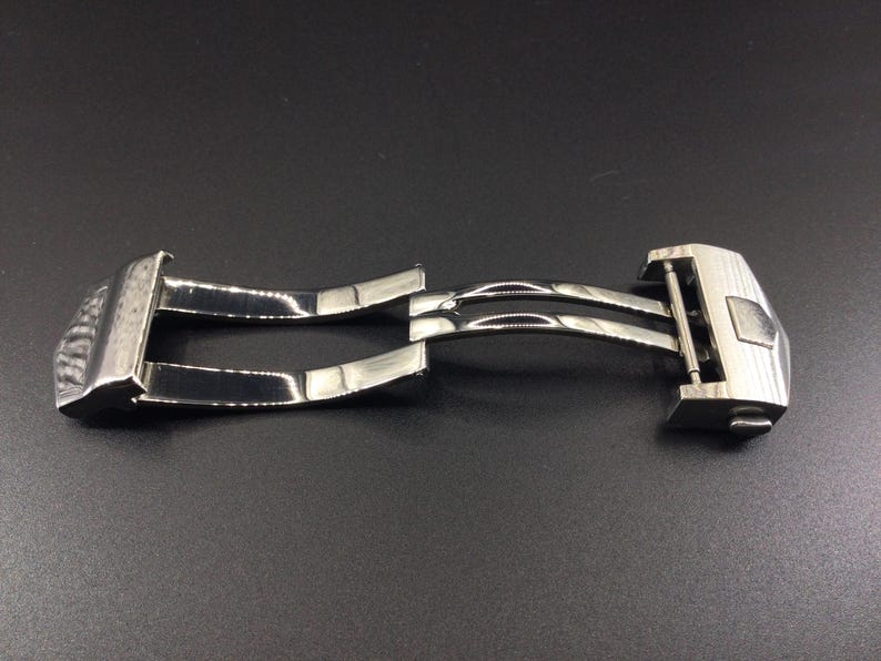 May include: A silver metal watch band clasp with a double-locking mechanism.