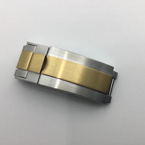 Puede incluir: Un cierre de correa de reloj de plata y oro con acabado pulido.